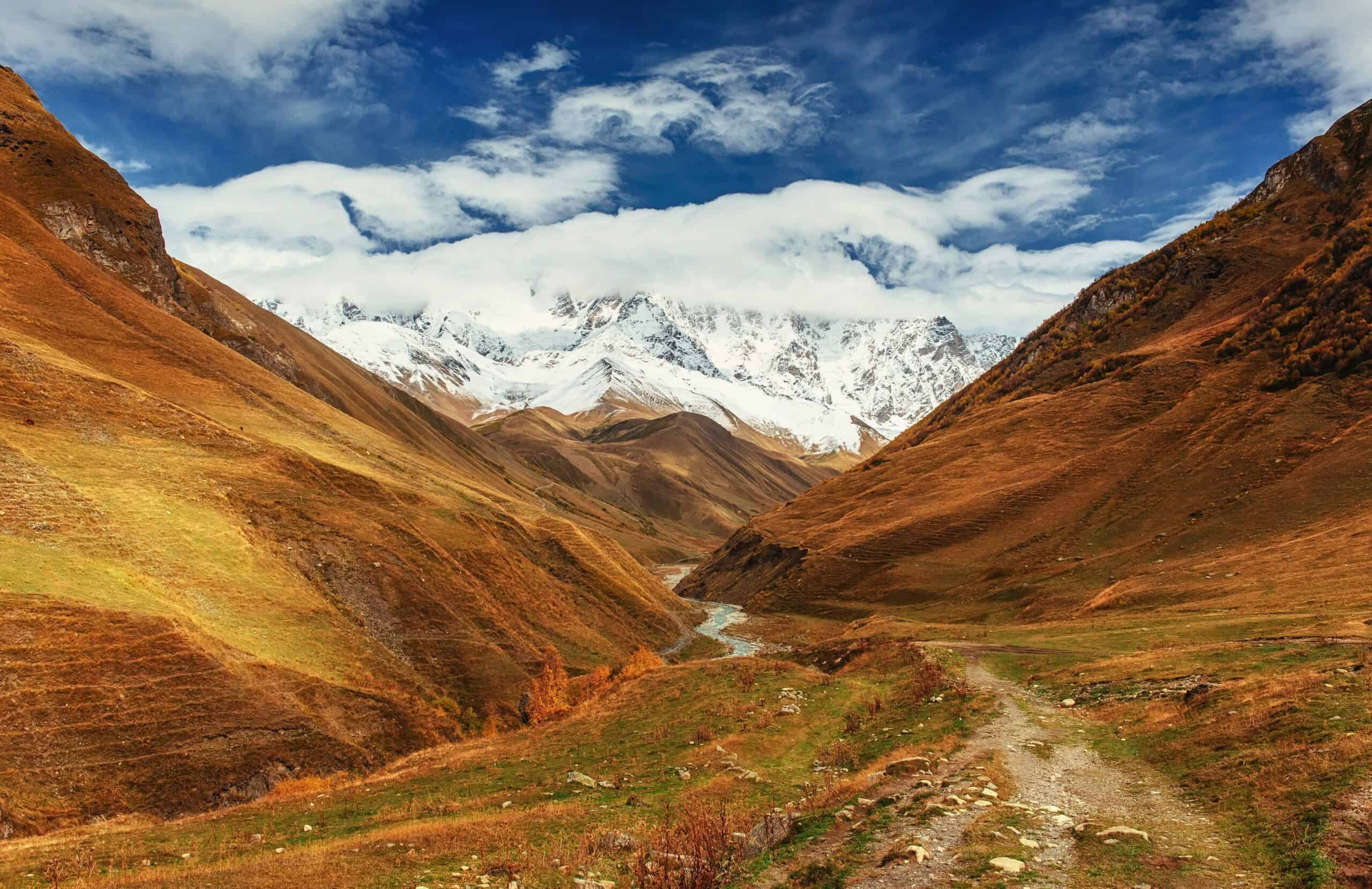 Mountain valley in Peru with a winding trail, river, and snow-capped peaks under a blue sky