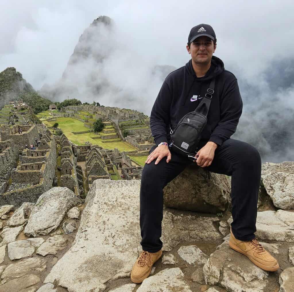 Traveler sitting above Machu Picchu with the ancient Inca ruins and misty mountains in the background, Peru