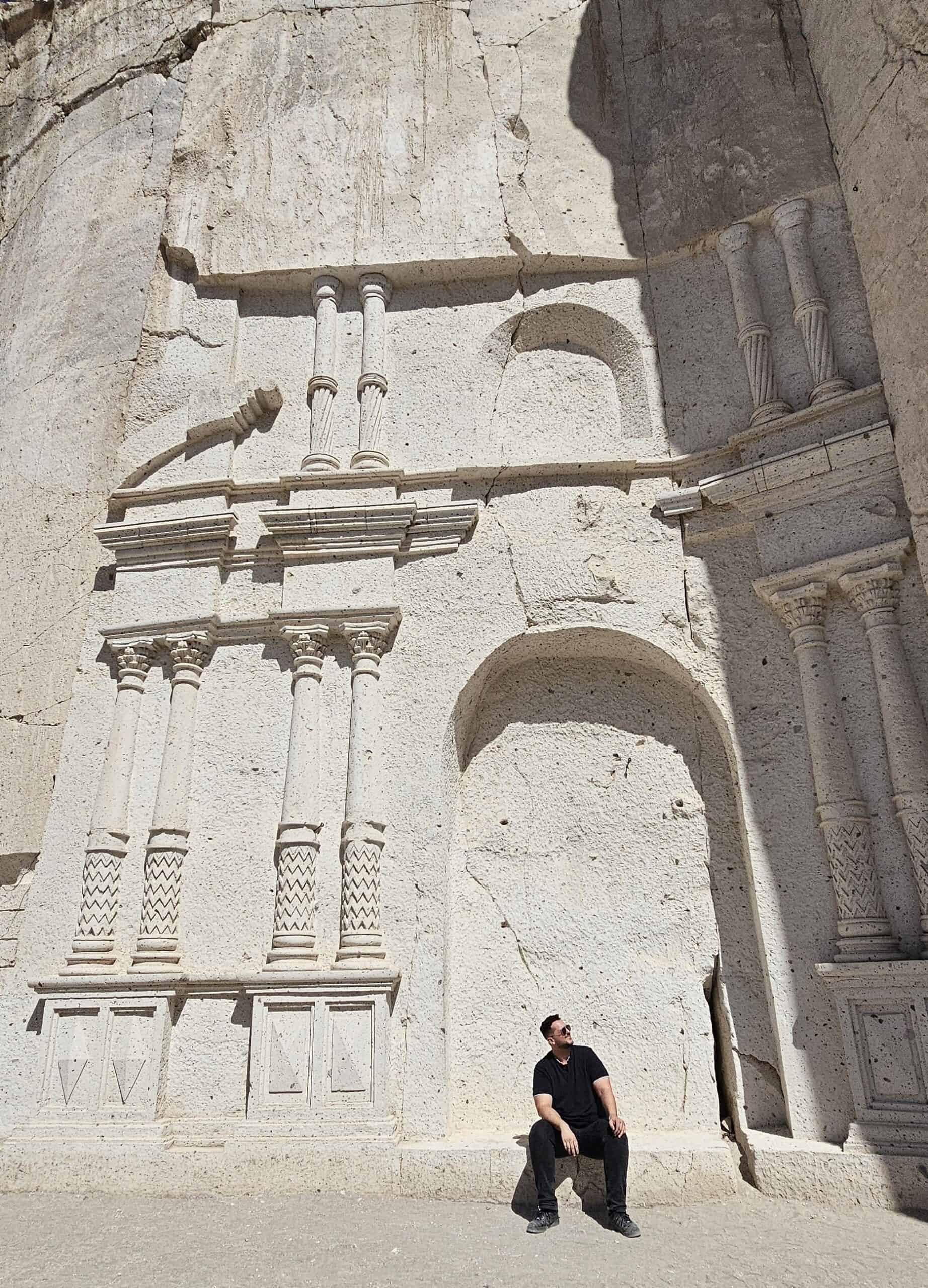 Me sitting in front of carved white volcanic stone walls on the Ruta del Sillar near Arequipa, Peru